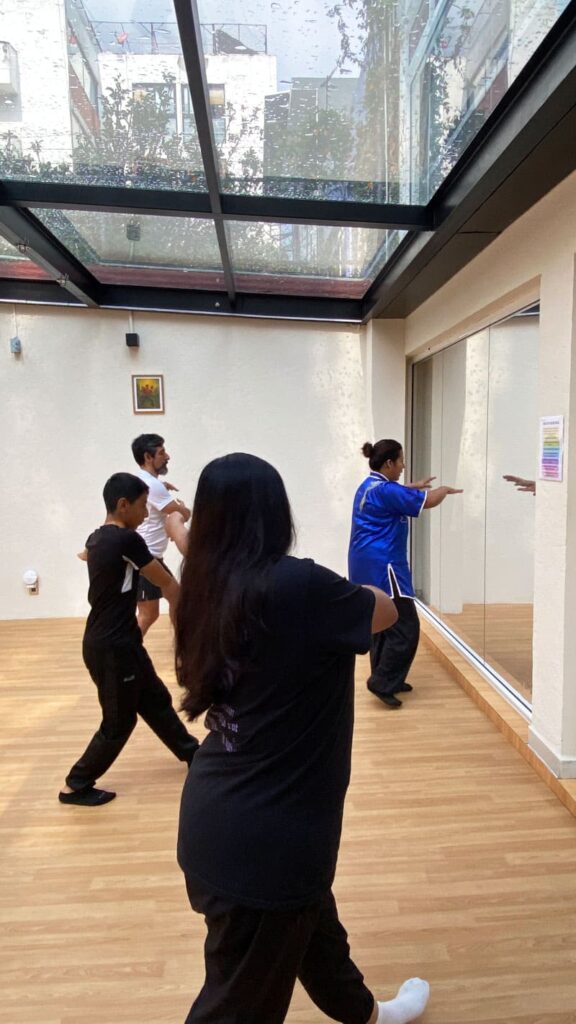 Clase de tai chi con instructor y alumnos realizando movimientos suaves en un salón amplio